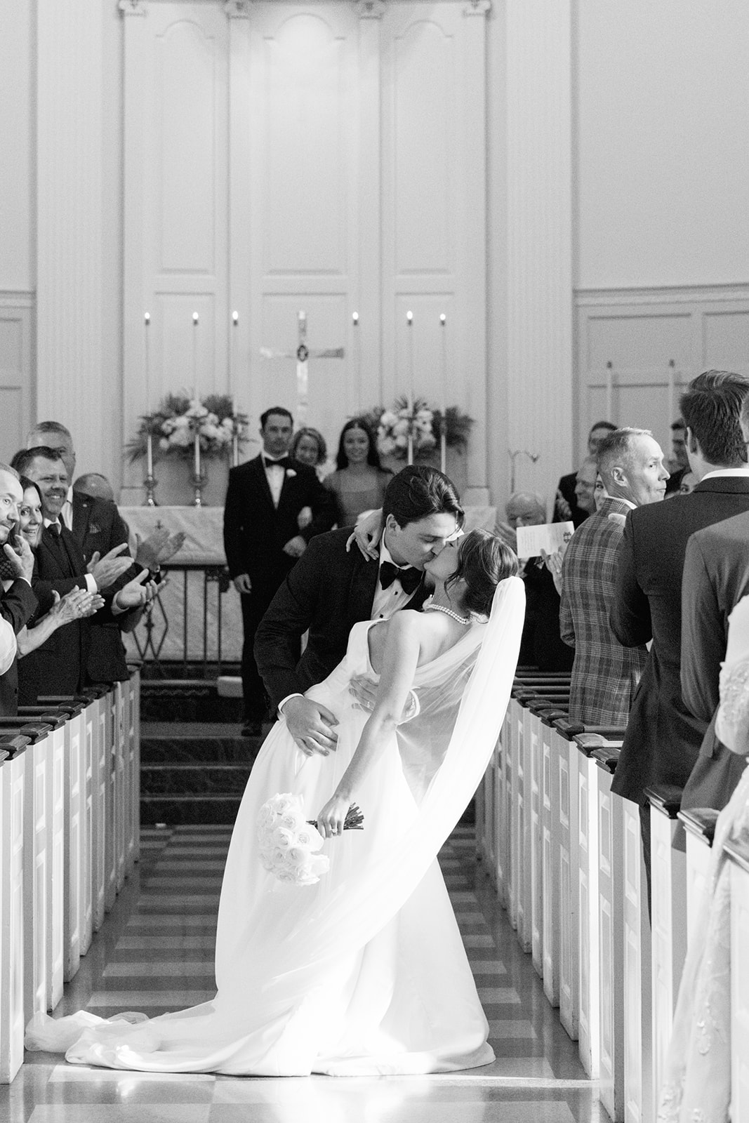 The groom dips the bride for a romantic kiss at the end of the ceremony aisle while guests cheer and applaud in celebration
