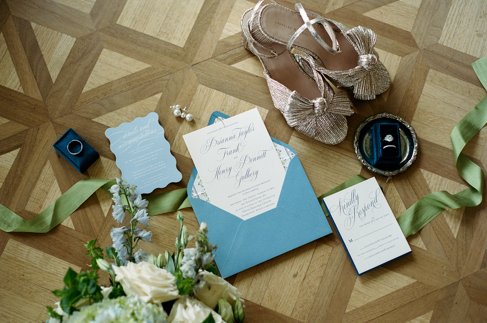 Film photograph of wedding invitations, rings, and gold bow heels styled with white roses and green ribbon.