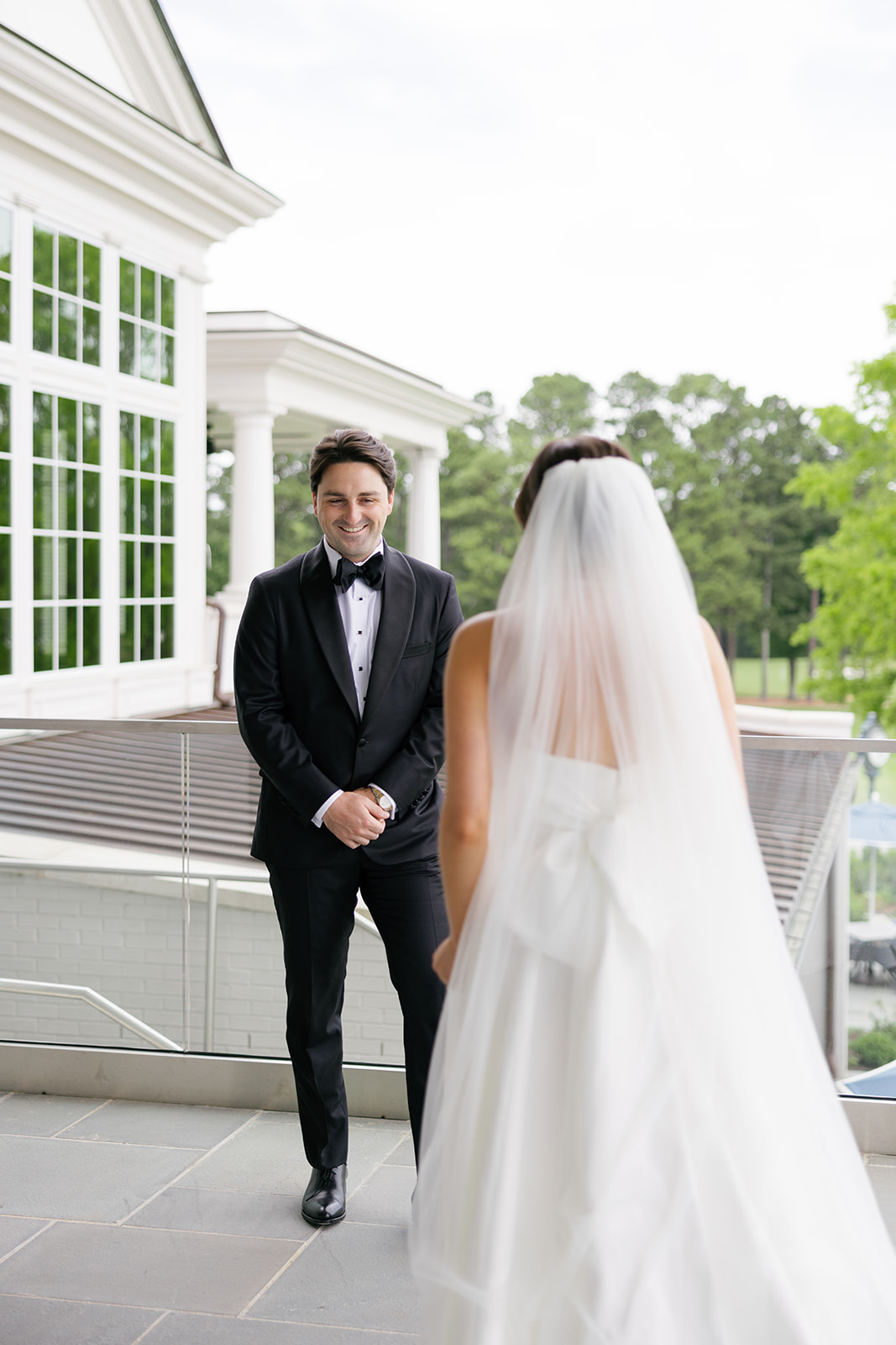 Groom smiling warmly at his bride during first look on the balcony.
