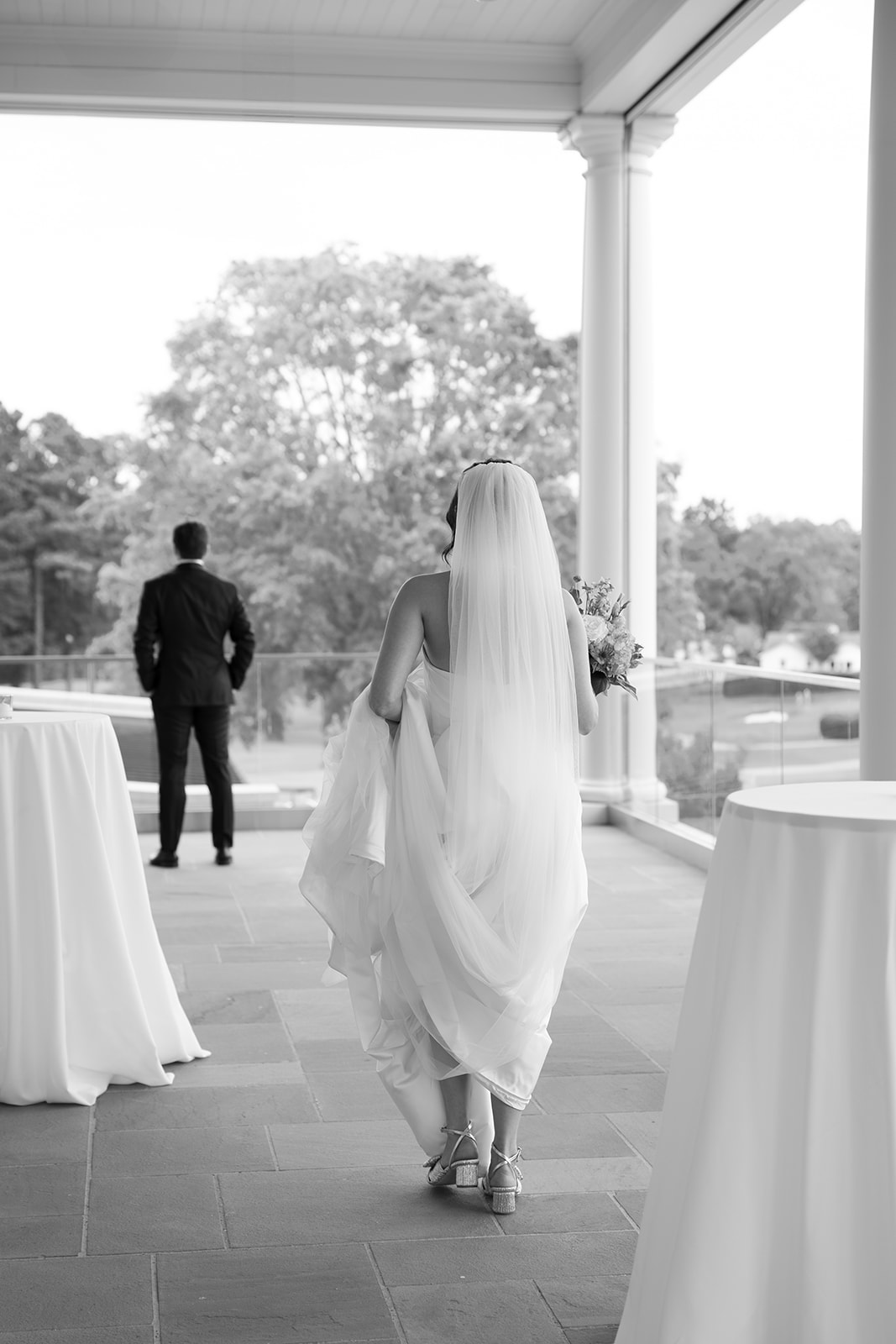 Bride in flowing veil walking toward groom for their first look on the balcony at Myers Park Country Club.
