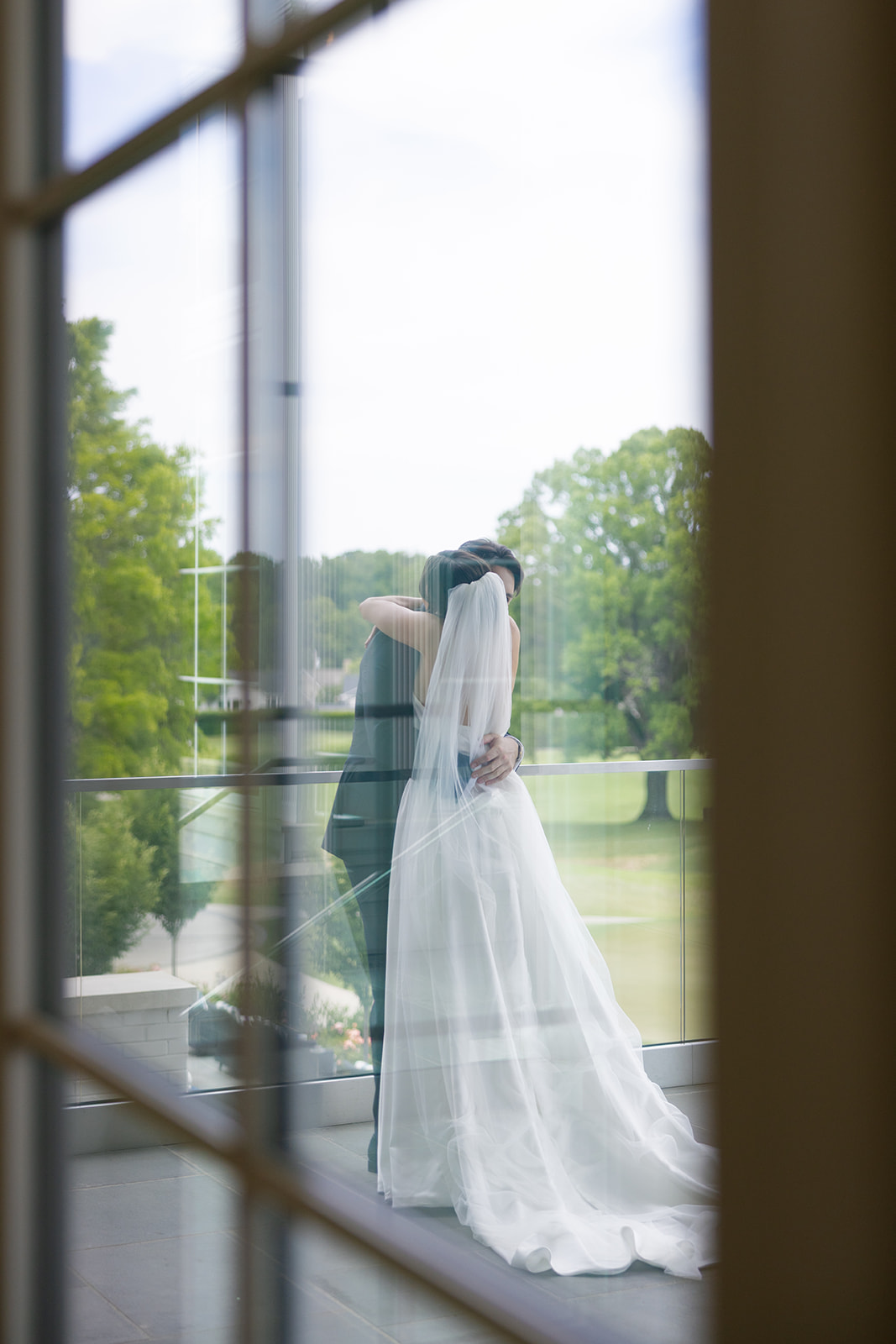 Emotional embrace between bride and groom during first look, captured through the window.