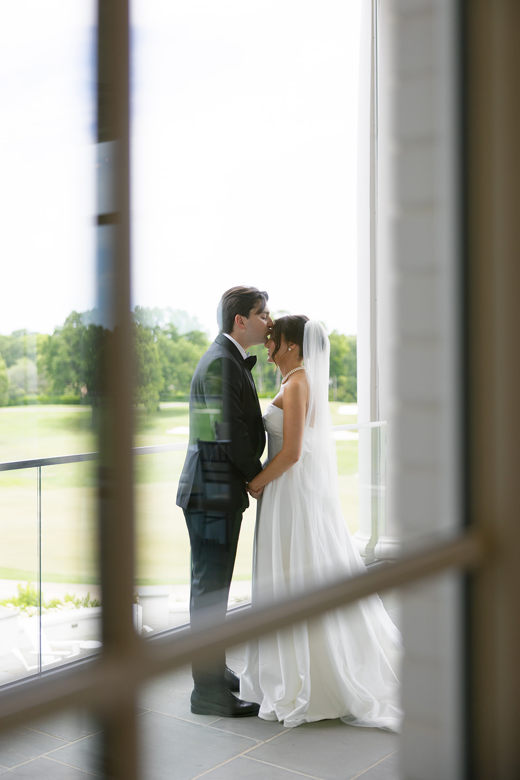 Groom kissing bride’s forehead as they hold hands during first look moment.