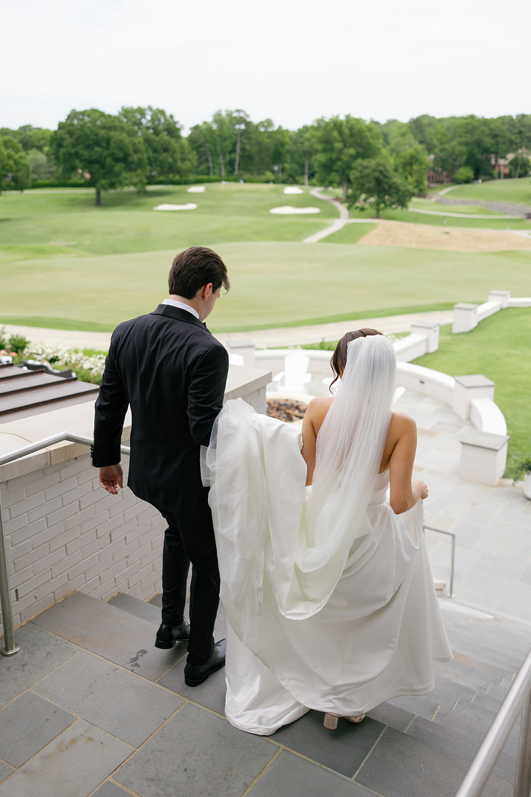 Bride and groom walking down the club’s terrace steps with golf course views in the background.