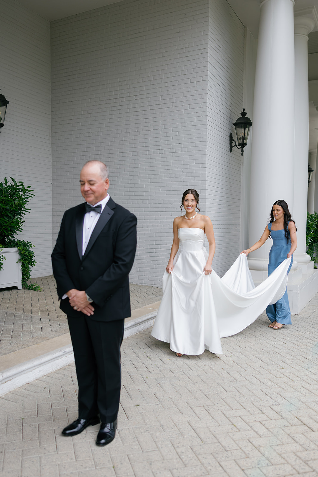 bridesmaid holds the bride's dress train as she gets ready for first look with her father