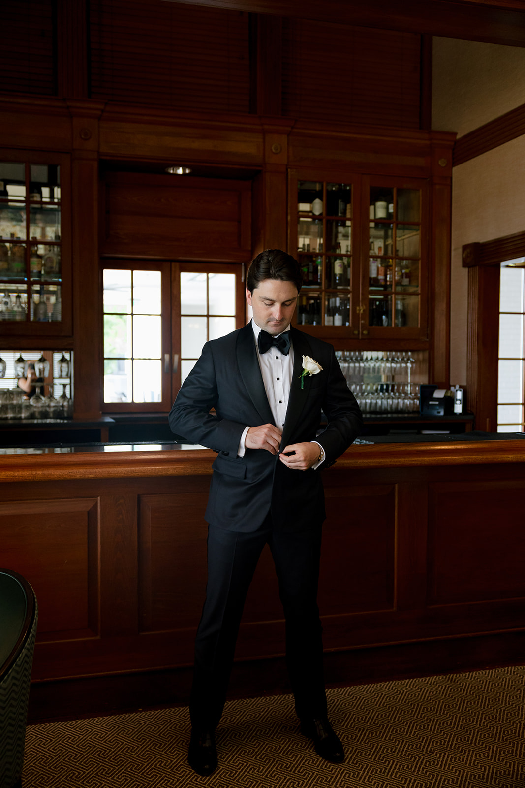 Groom adjusting his buttons in a black tuxedo with a white rose boutonniere at Myers Park Country Club.