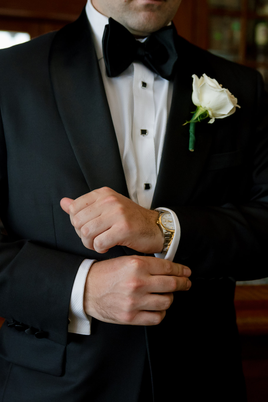Groom adjusting his sleeves in a black tuxedo with a white rose boutonniere at Myers Park Country Club.
