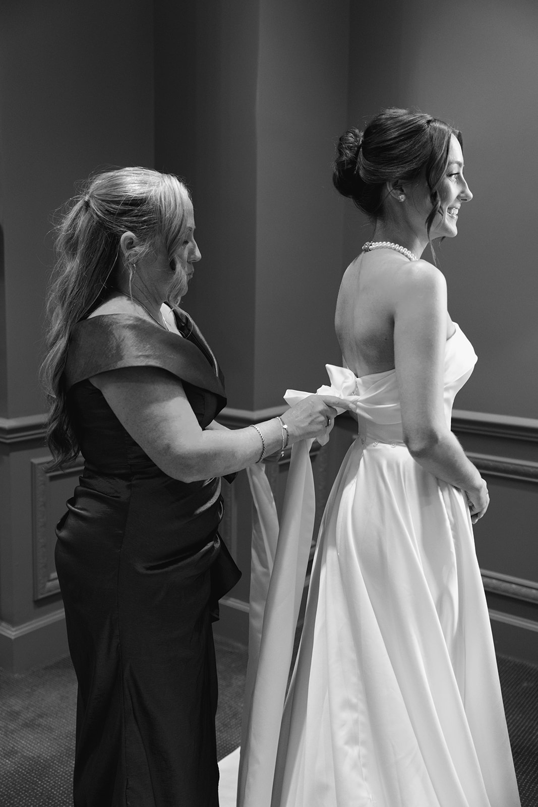Black and white wedding photography showing the bride’s dress being tied with a bow before the ceremony at Myers Park Country Club.