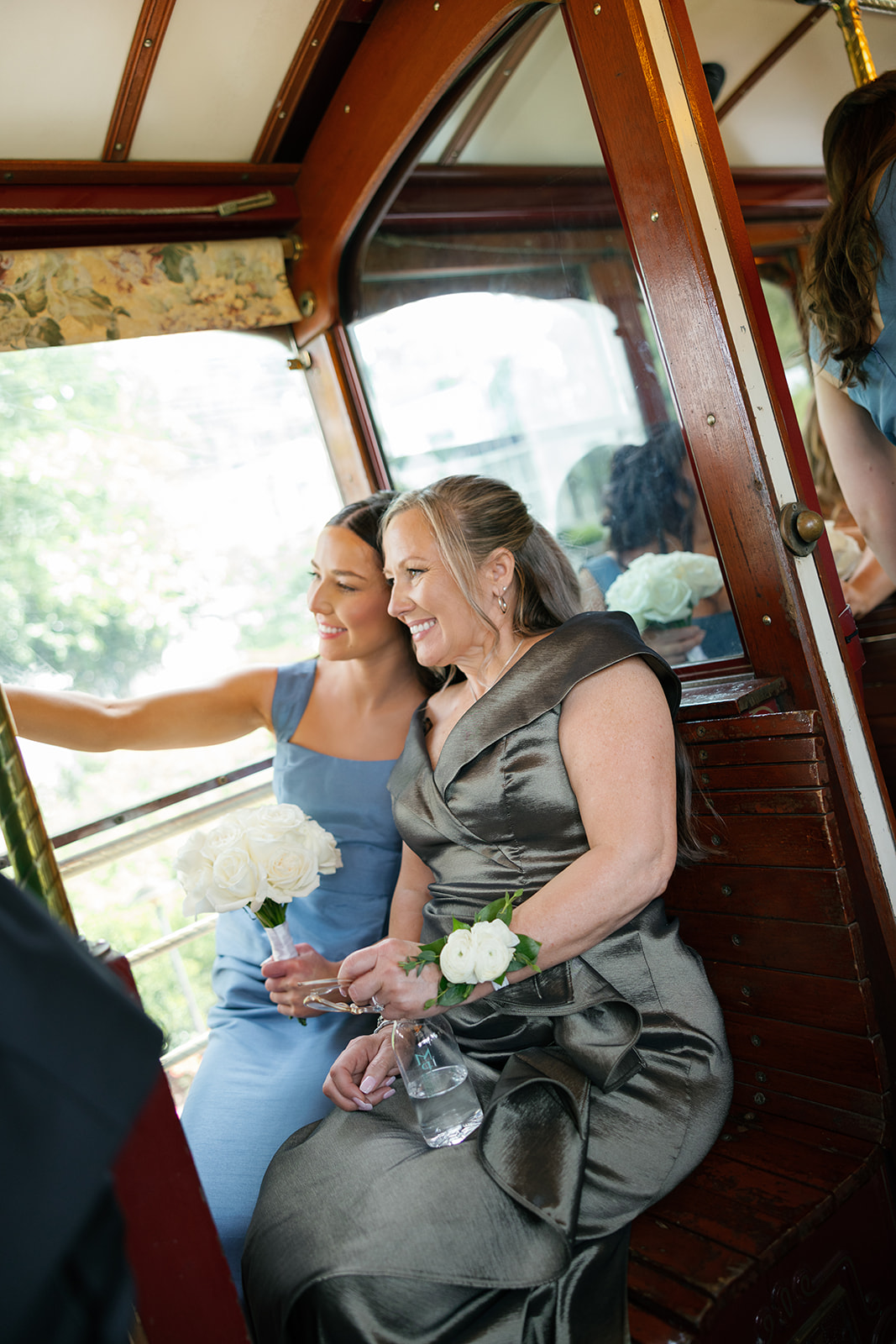 Bridesmaid in a dusty blue dress taking a photo with the wedding party inside a trolley.