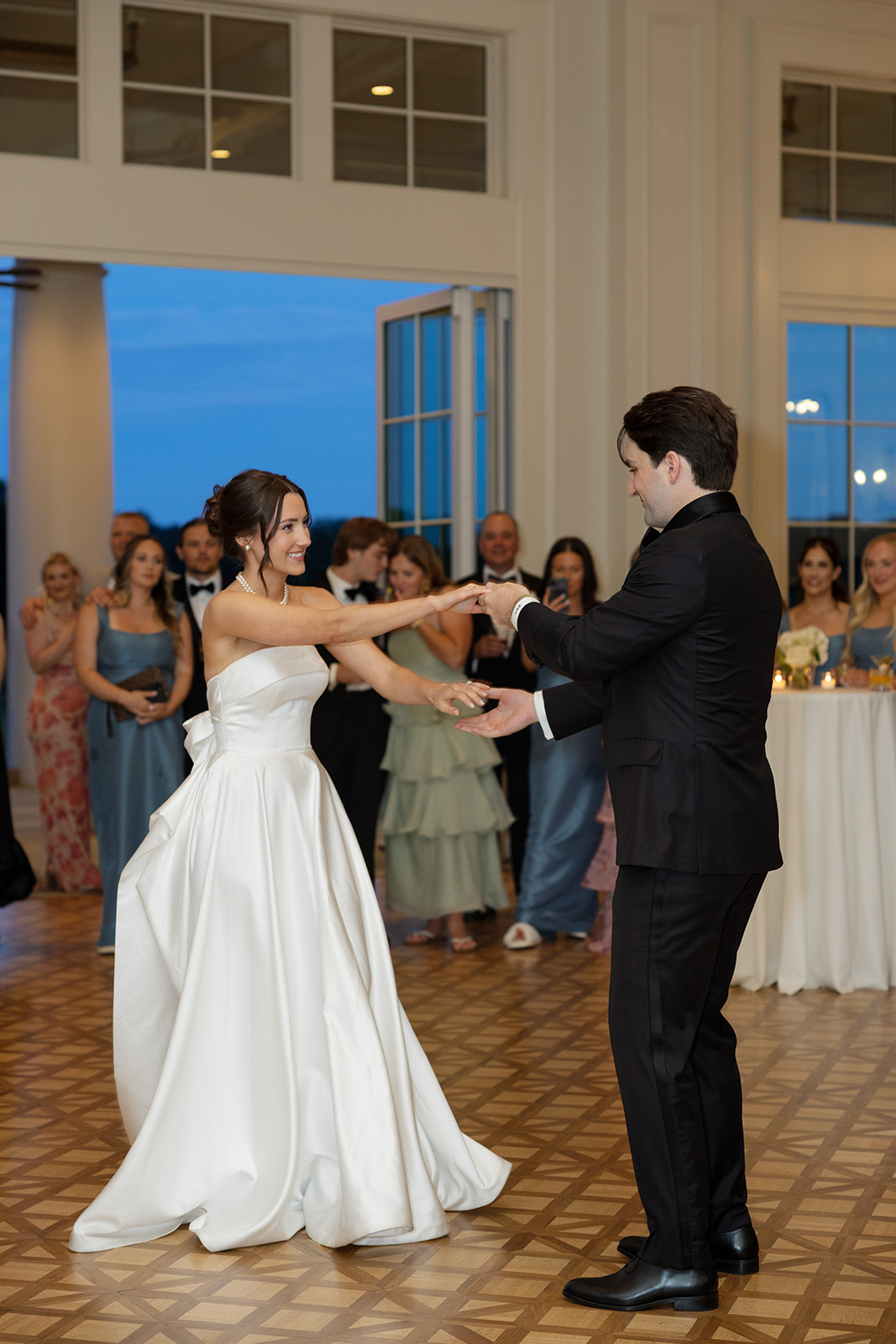 Groom and bride on the dance floor during their first dance, her gown flowing as guests watch.