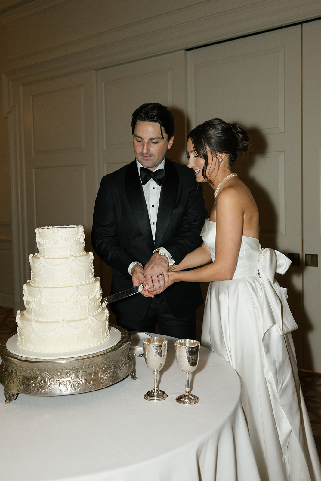 Bride and groom share a laugh while cutting their elegant tiered wedding cake together.