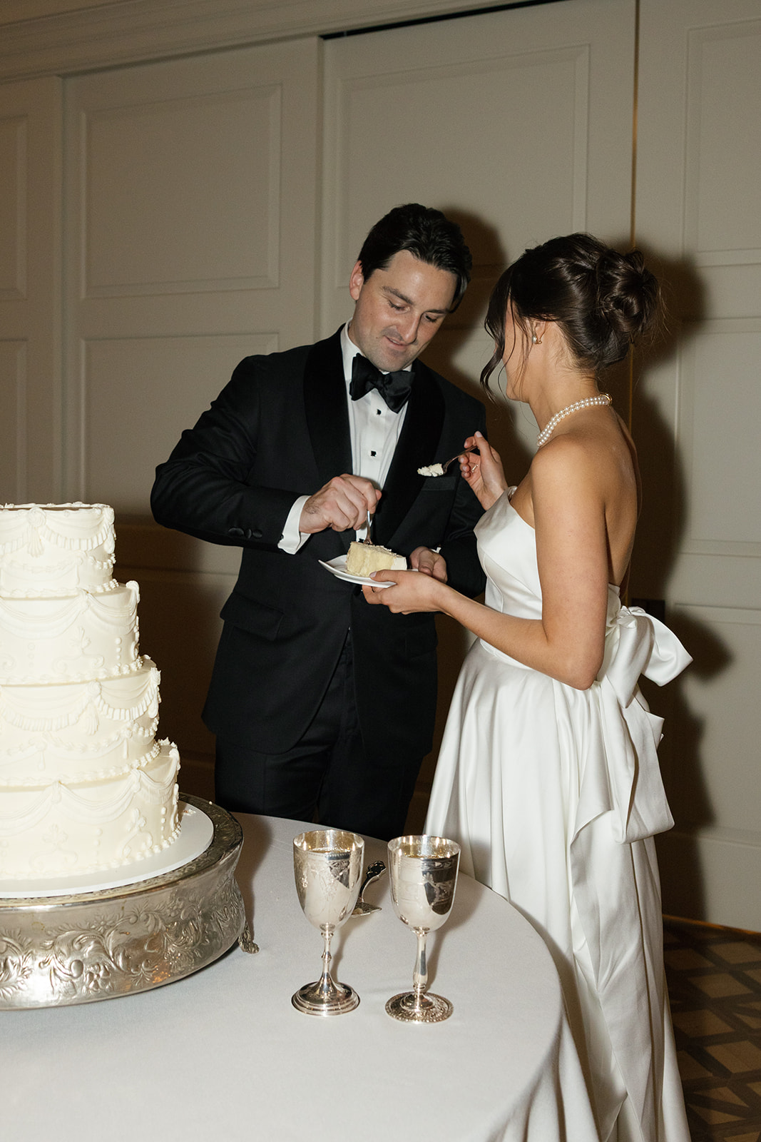 Groom feeds the bride a bite of wedding cake as they smile at each other.