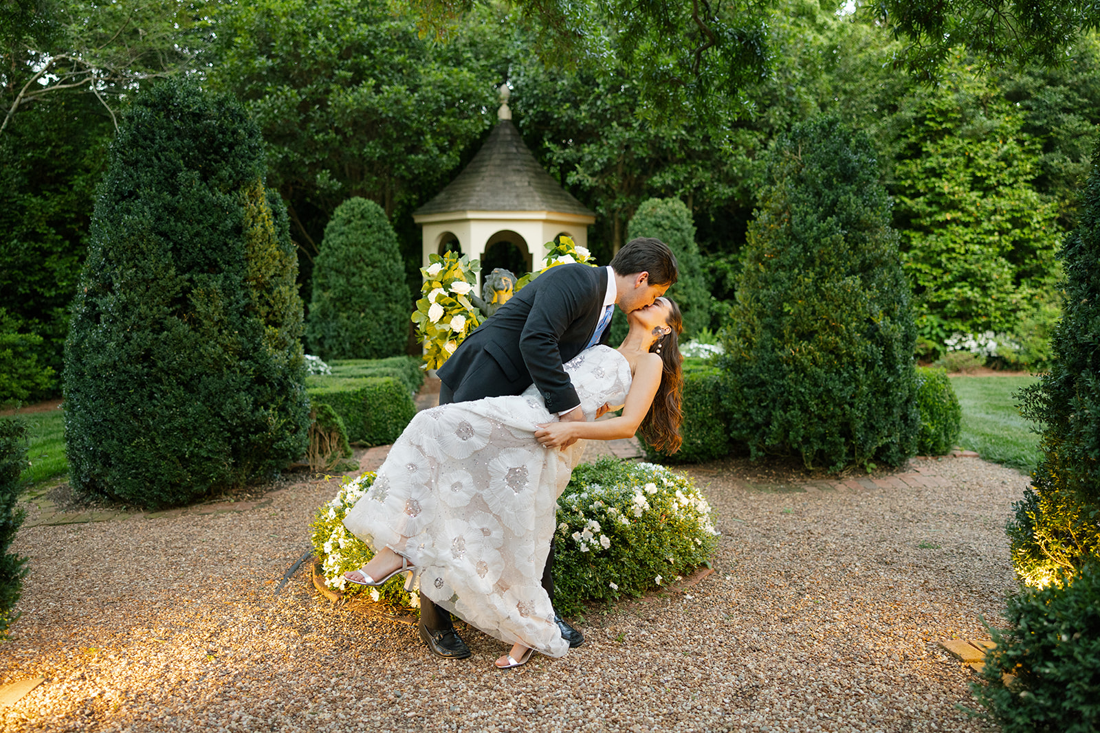 Groom dipping bride for a kiss in the garden at their North Carolina welcome party, included in their wedding photography package.