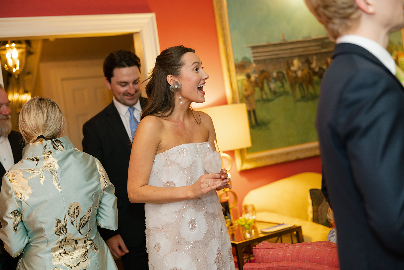 Bride in a strapless white gown smiling with guests at the welcome party inside a North Carolina home.