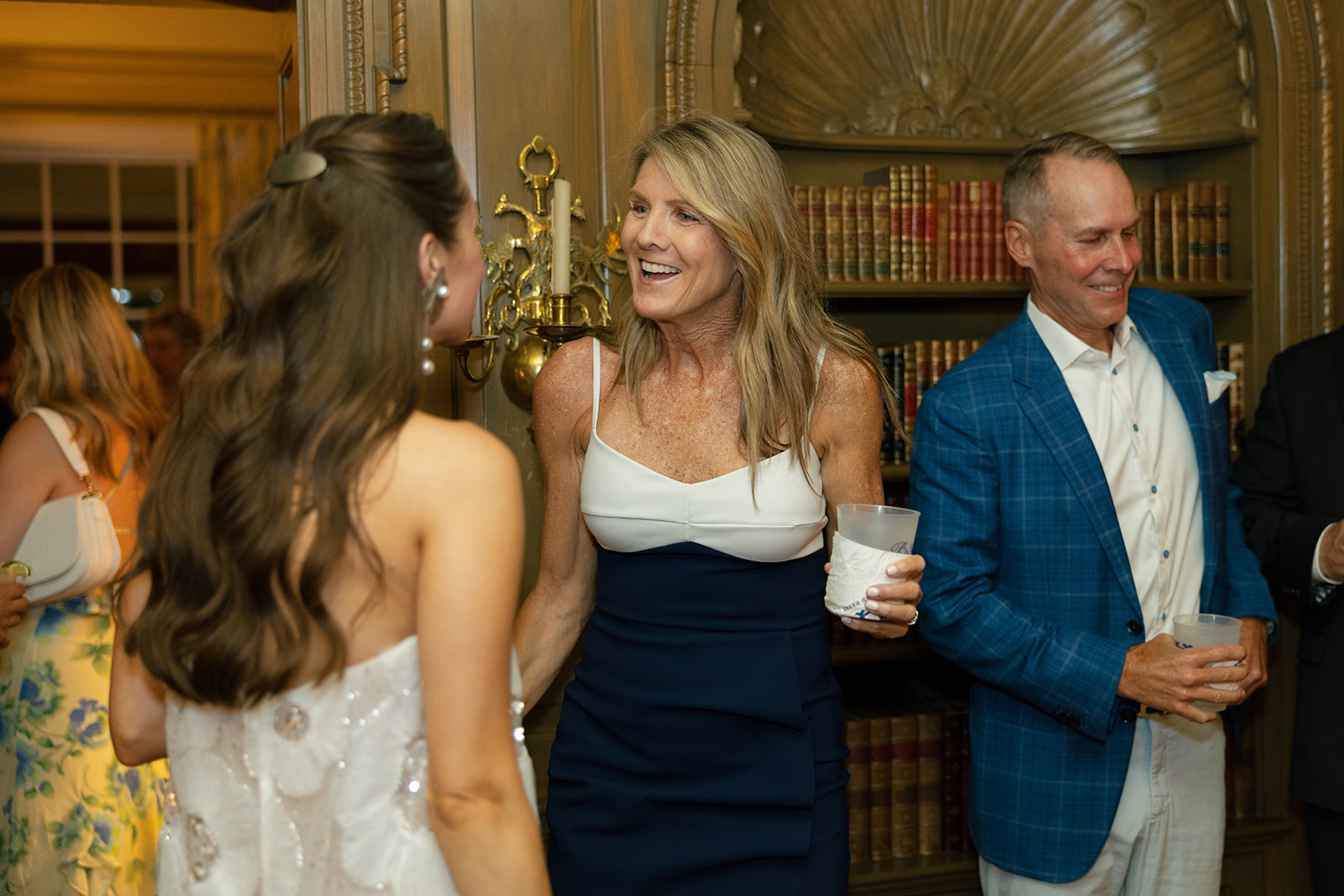 Bride chatting with guests in a cozy library setting at the welcome party in North Carolina, captured as part of a wedding photography package.