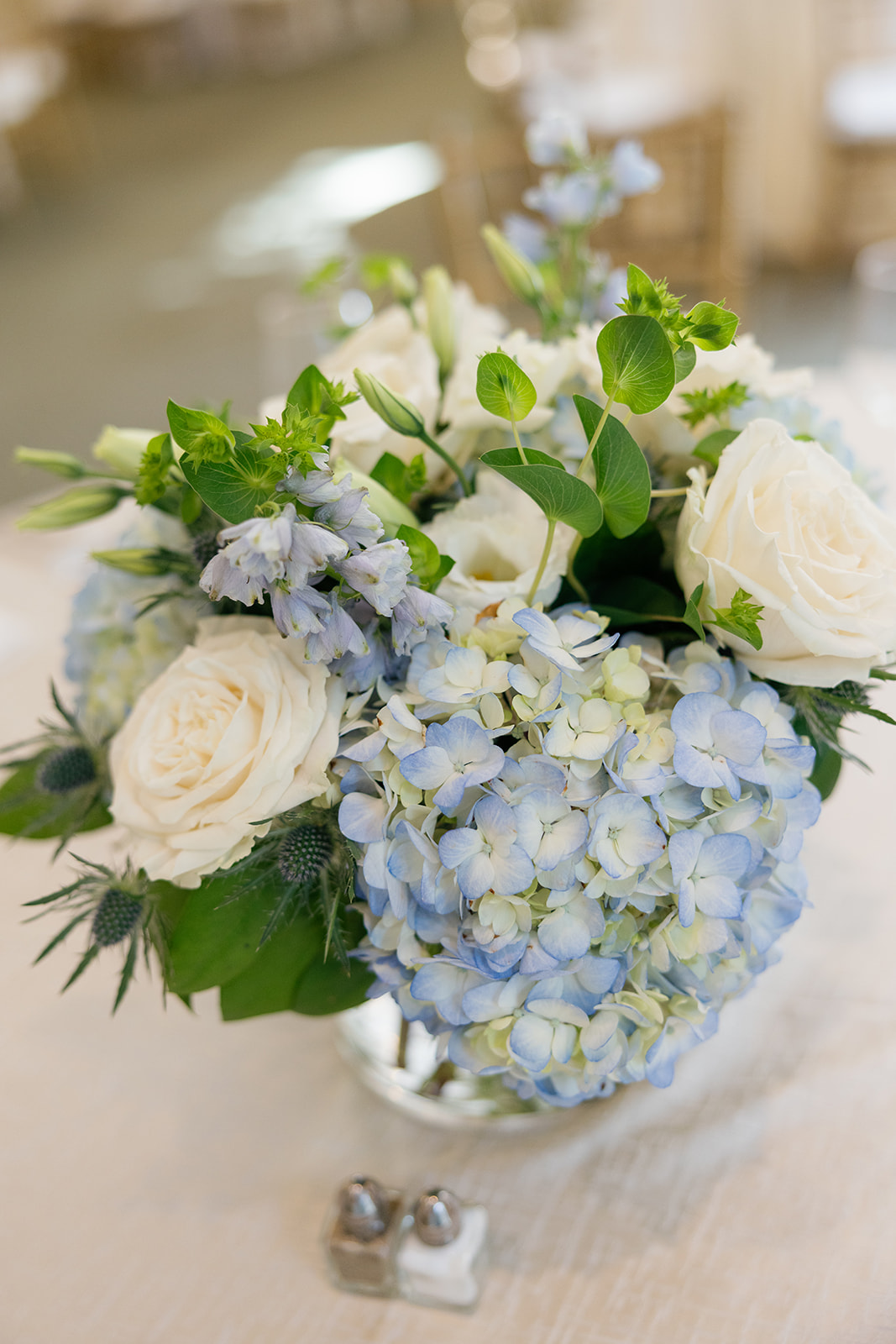 Elegant floral centerpiece of white roses and blue hydrangeas at Bri and Henry’s rehearsal dinner at Duke Mansion in Charlotte, NC.