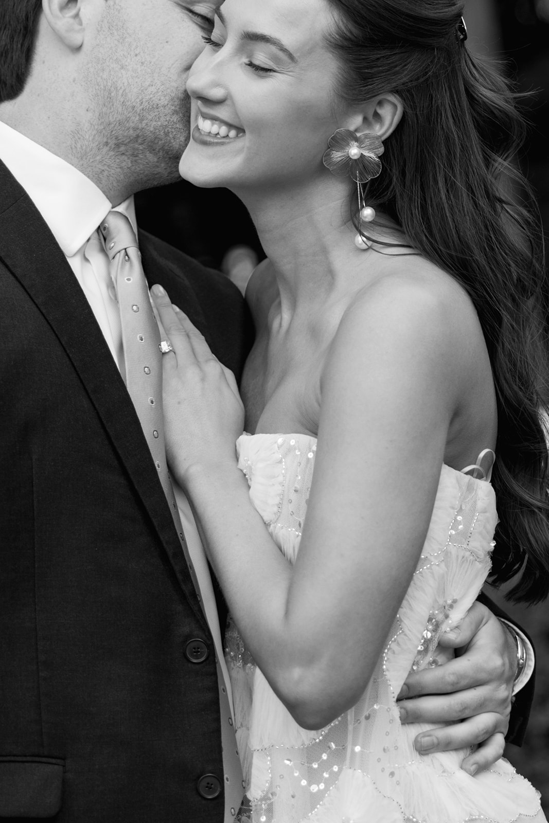 Romantic black and white close-up of a bride smiling as her groom kisses her cheek, captured at Duke Mansion rehearsal dinner.