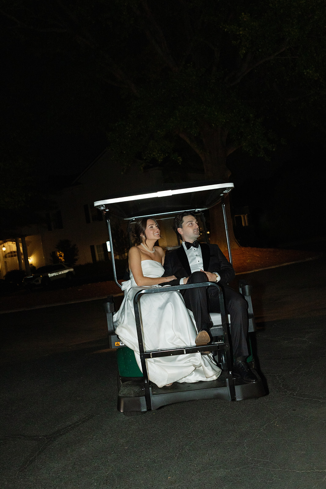 Bride and groom ride away in a golf cart, smiling and looking back.