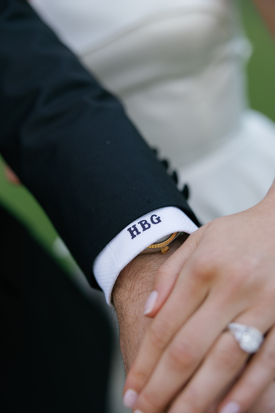 Close-up of the groom’s cuff embroidered with his initials “HBG,” as he holds the bride’s hand, showcasing her diamond engagement ring.