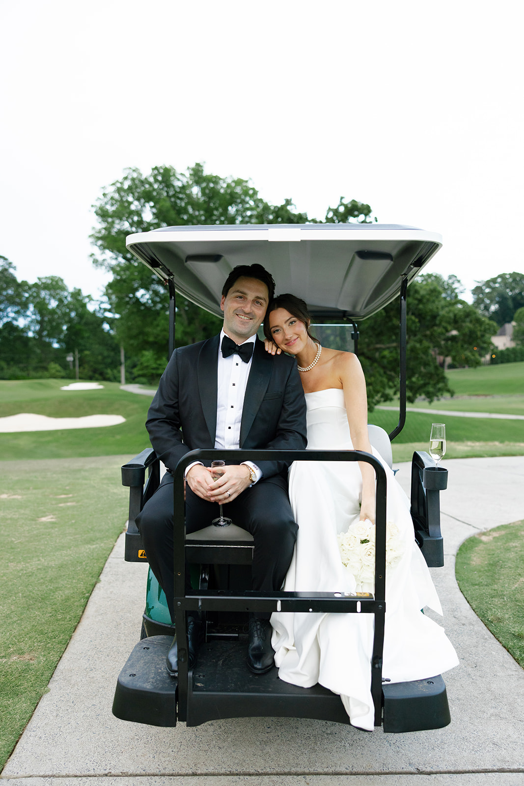 Bride leans her head on the groom’s shoulder as they sit together on a golf cart during sunset portraits