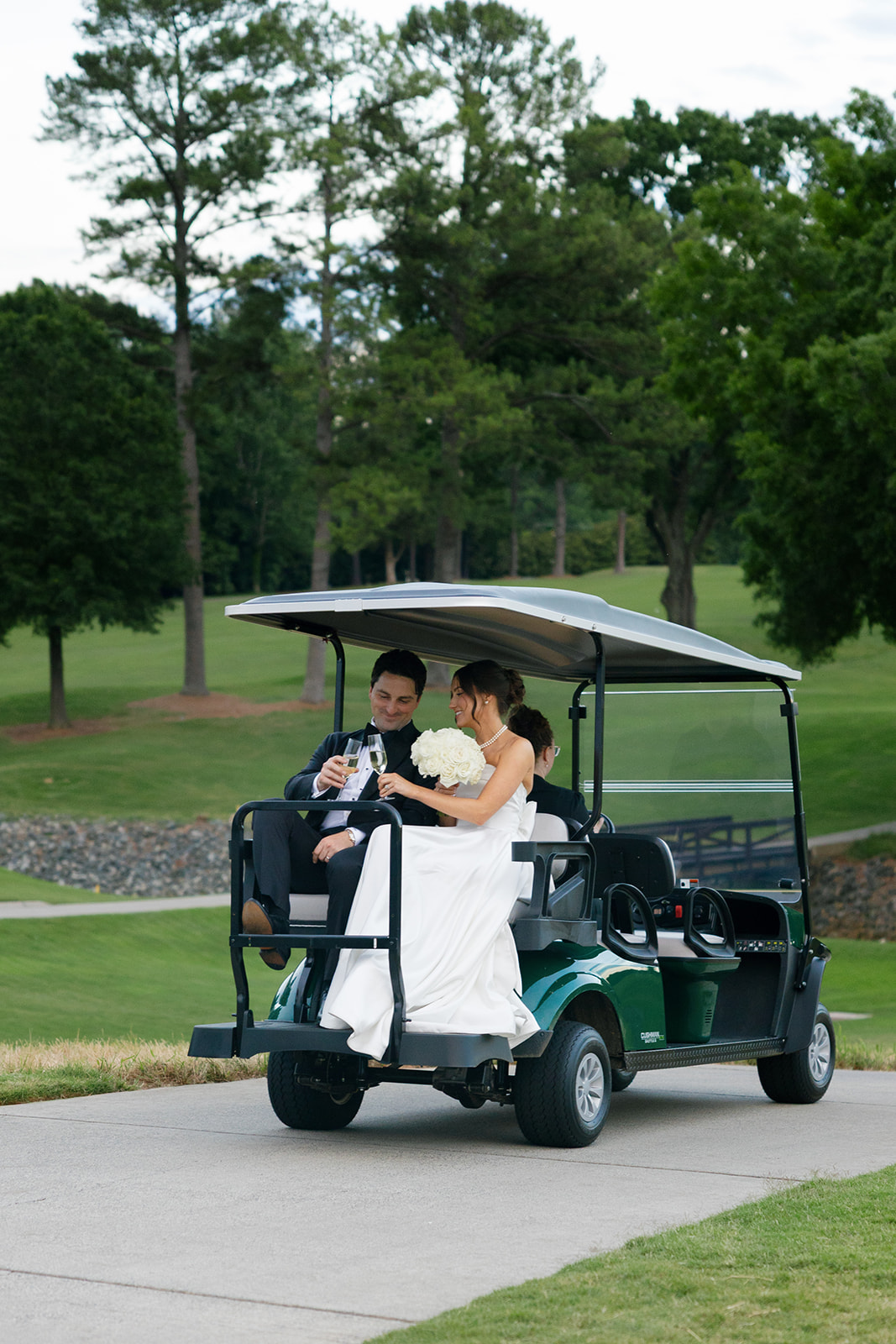 Bride and groom clink champagne glasses while riding a golf cart at Myers Park Country Club after their ceremony.