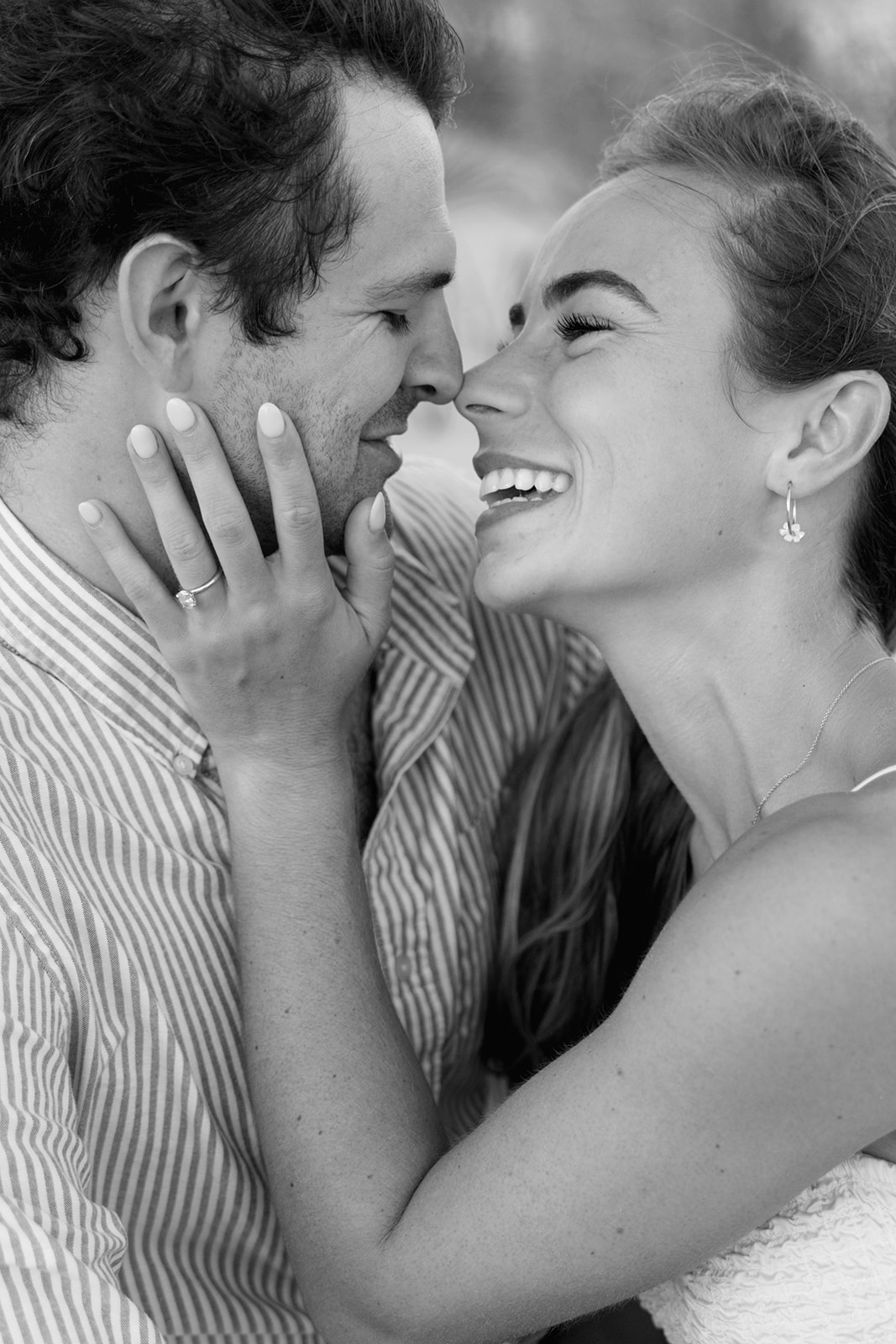 Romantic black and white close-up of a woman laughing while holding her fiancé’s face, their noses nearly touching during a Sullivan’s Island engagement session in Charleston SC.