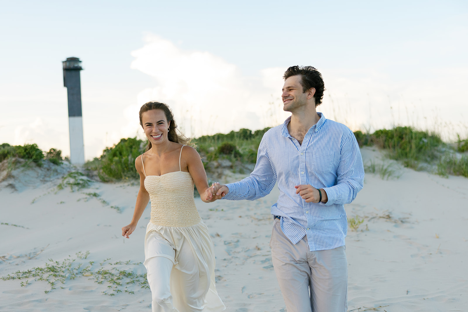 Close-up of the couple smiling while running hand in hand along the beach dunes, captured by a Charleston SC engagement photographer at Sullivan’s Island.