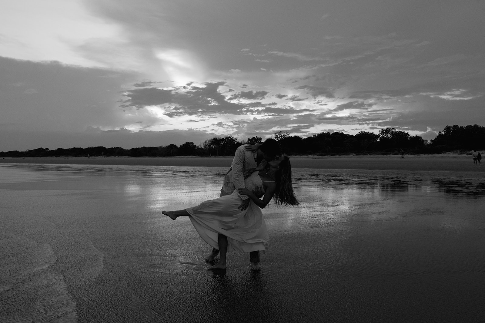 Couple sharing a romantic dip and kiss on the shoreline during their Charleston SC engagement session at Sullivan’s Island, captured by a Charleston SC engagement photographer.