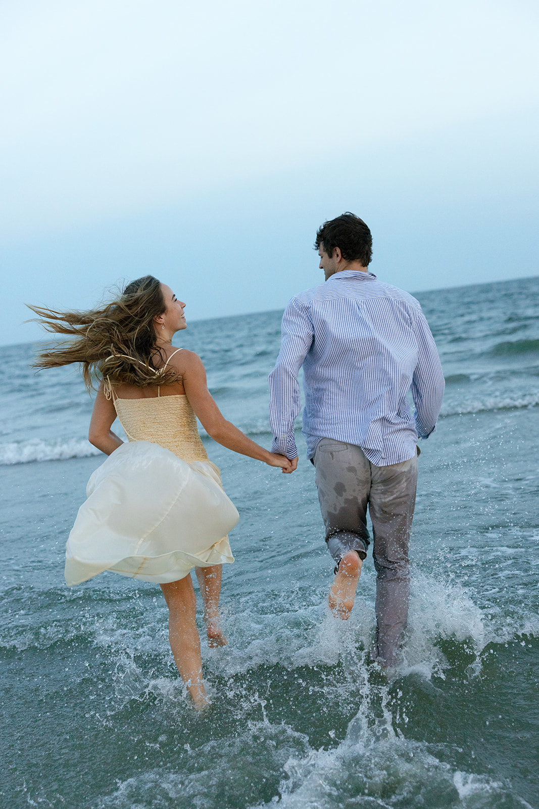 Playful moment of couple running through the waves together in their Charleston SC engagement photos