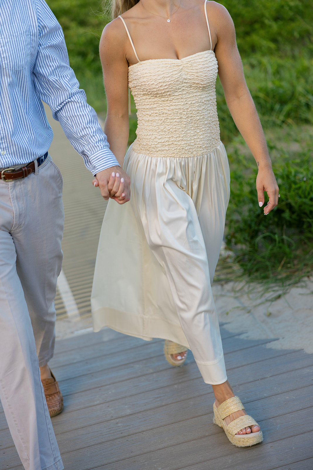 Couple holding hands and walking down a wooden boardwalk surrounded by greenery, captured by a Charleston SC engagement photographer.