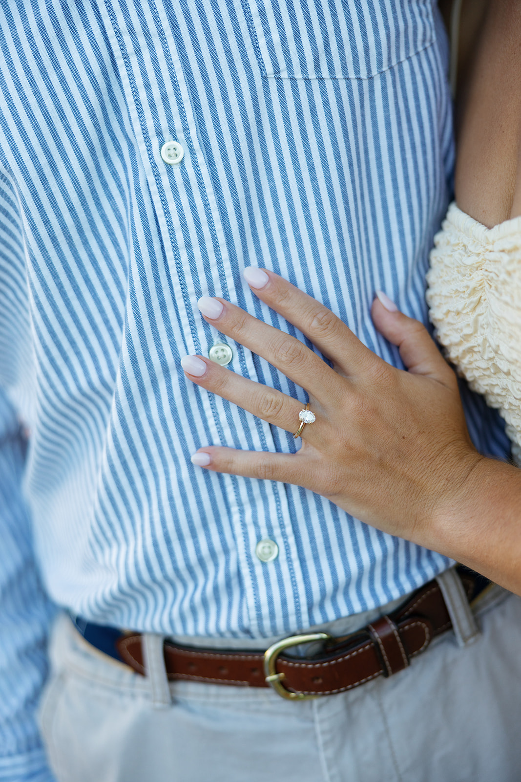 Close-up of an engagement ring on her hand resting against her partner’s striped blue shirt during a Charleston SC engagement session at Sullivan’s Island.
