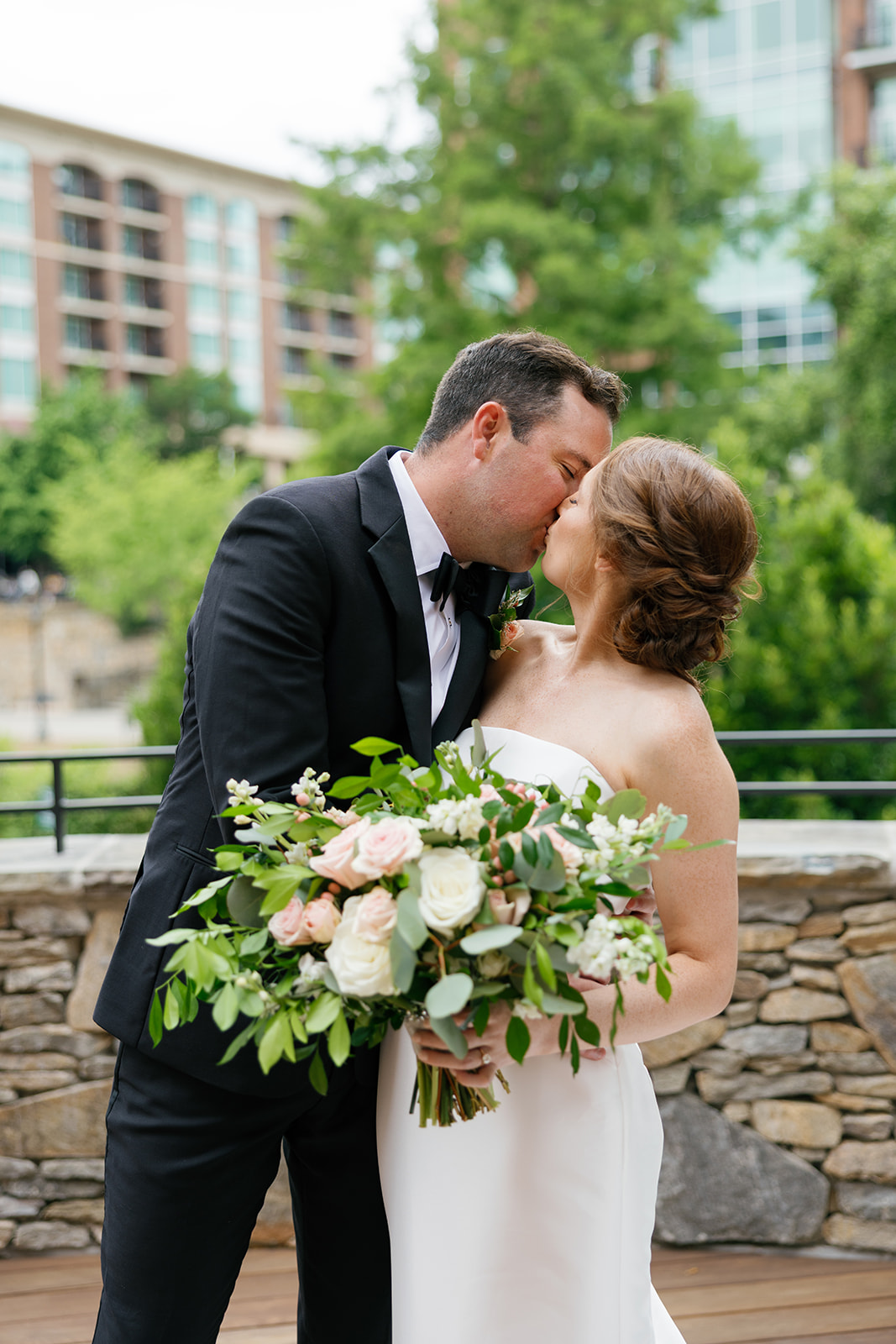 Bride and groom sharing a kiss while holding a classic bouquet of roses and greenery at their Greenville, SC wedding.