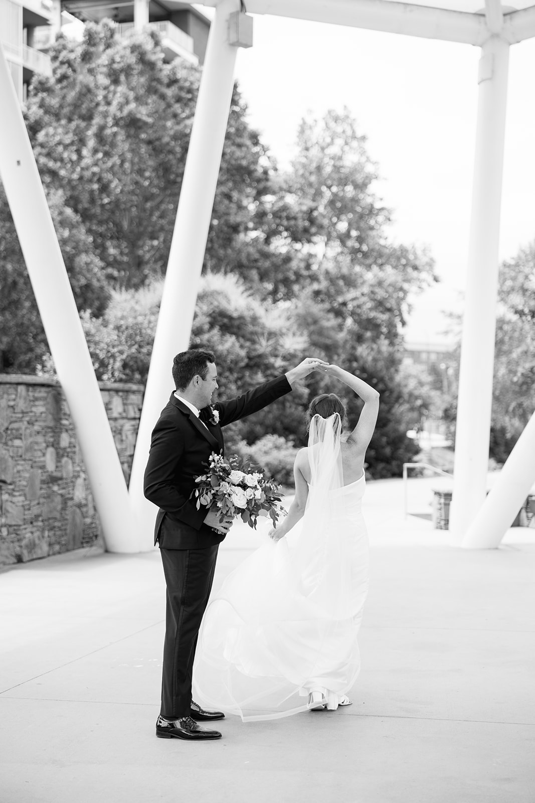Black and white photo of the groom twirling the bride beneath a modern white structure in downtown Greenville.