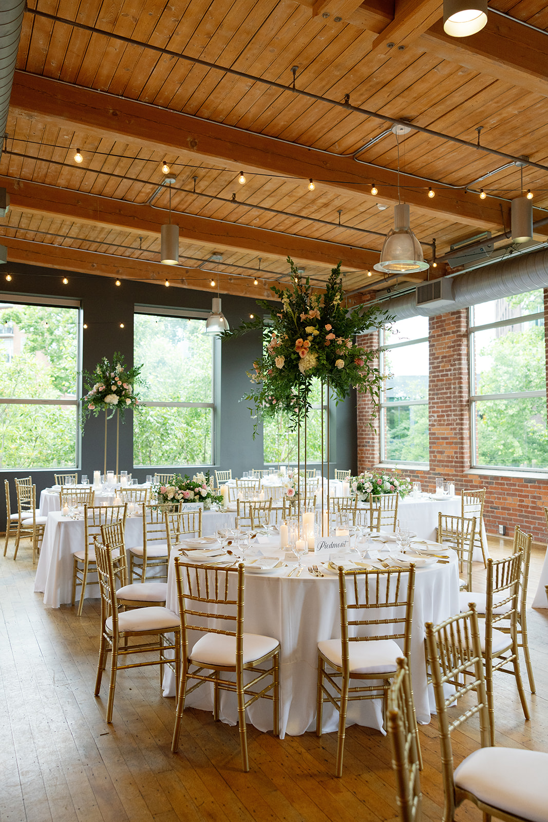 Round wedding reception table with tall greenery centerpiece and candles at Huguenot Loft and Mill in Greenville SC.