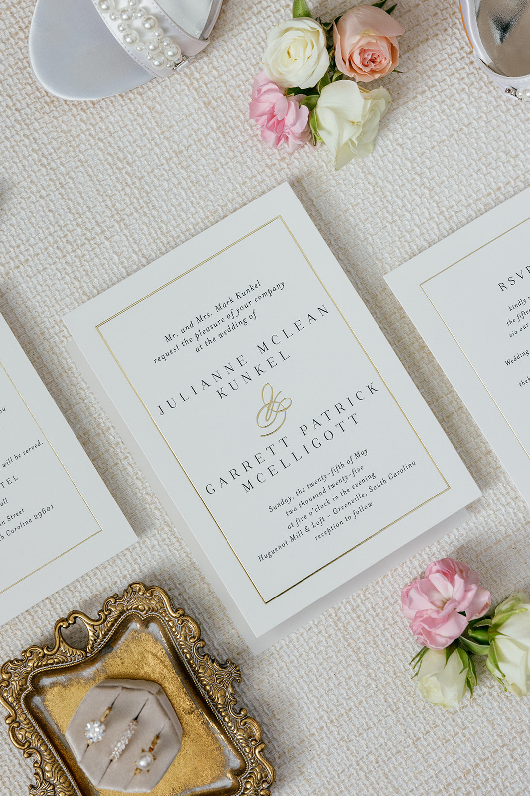 Elegant wedding invitation suite with gold trim, bridal shoes, and pastel flowers styled for a flatlay detail photo.