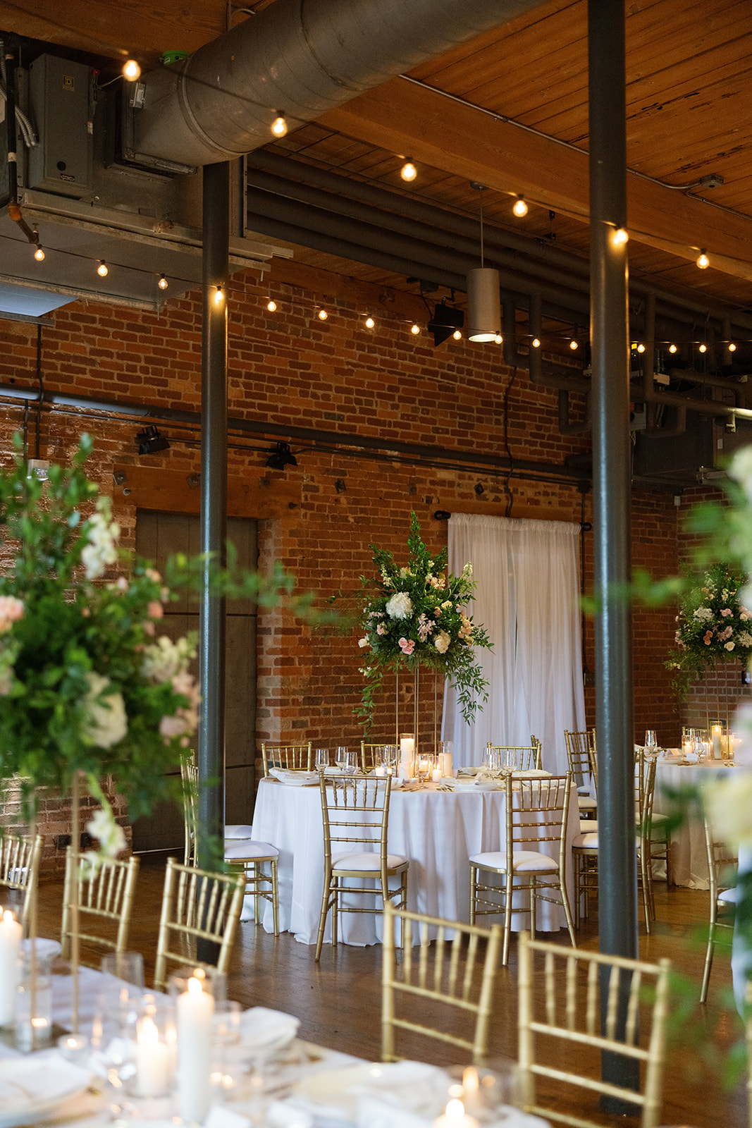 Elegant reception setup with tall floral centerpieces and glowing candles at Huguenot Loft and Mill, a Greenville SC wedding venue with exposed brick walls.