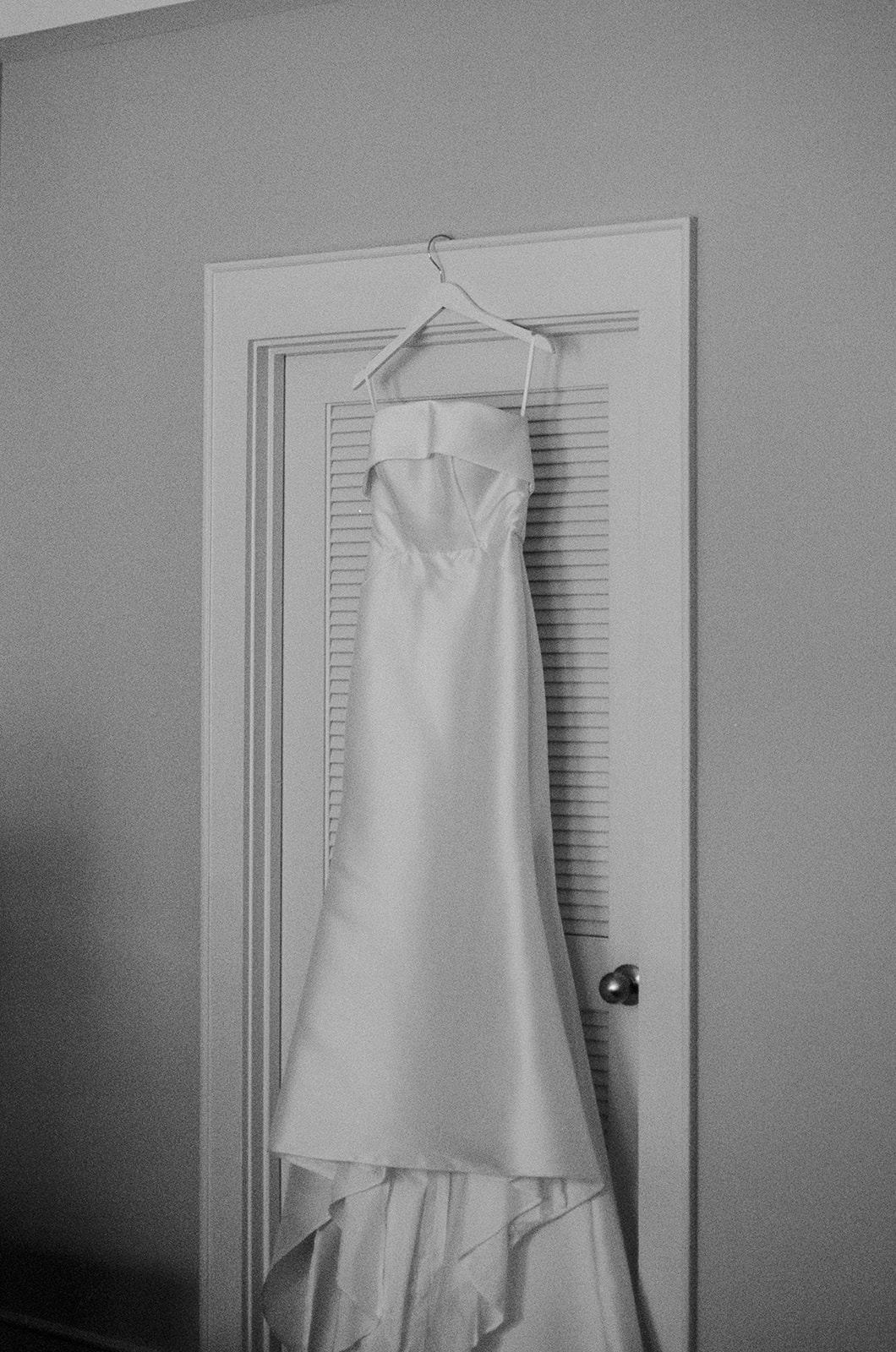 Strapless satin wedding gown hanging on a door before the ceremony at Huguenot Loft and Mill in Greenville SC.