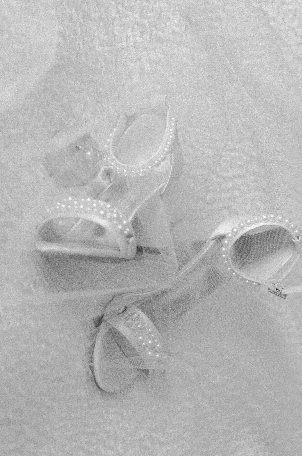 White bridal heels with pearl straps photographed through delicate tulle before the wedding at Huguenot Loft and Mill in Greenville SC.