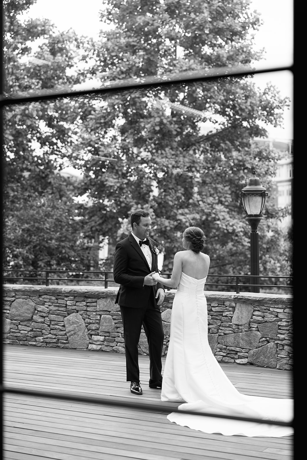 Black and white photo of bride and groom during their first look, framed through a window at Huguenot Loft in Greenville, SC.