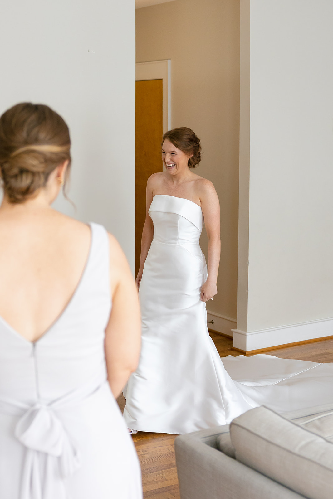 Bride in strapless gown showing her dress to bridesmaids during first look.