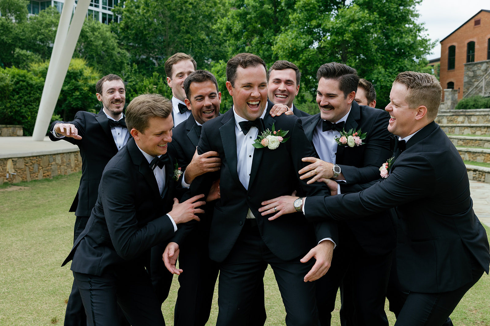 Groom laughing as his groomsmen surround him in a playful group photo outside Huguenot Loft in Greenville SC.