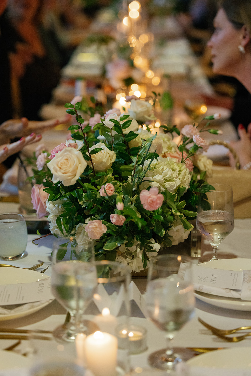 Elegant floral centerpiece of roses, hydrangeas, and greenery on a candlelit reception table at Huguenot Loft.