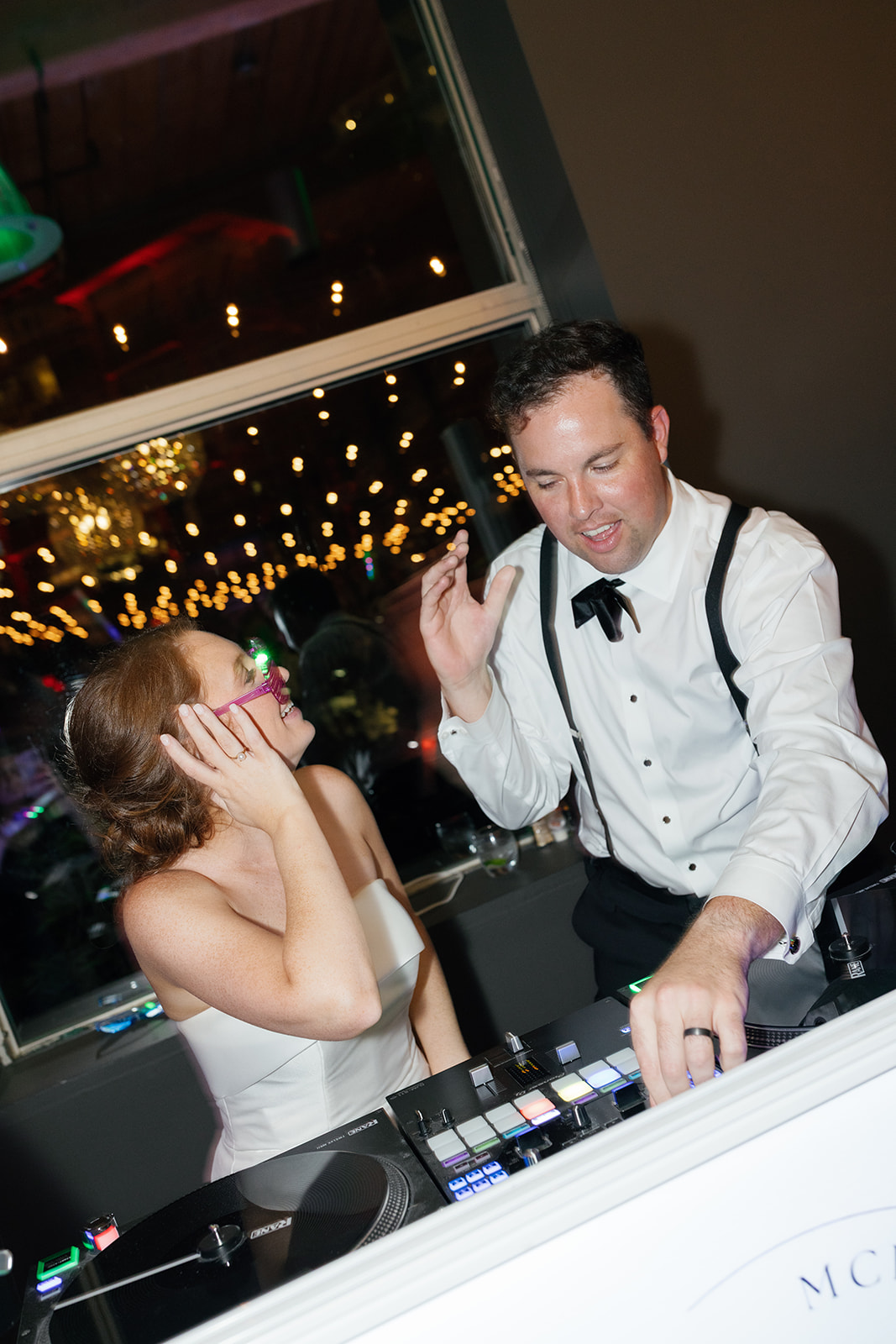 Bride joins the groom at the DJ booth during their reception, laughing while he pretends to spin music at Huguenot Loft.