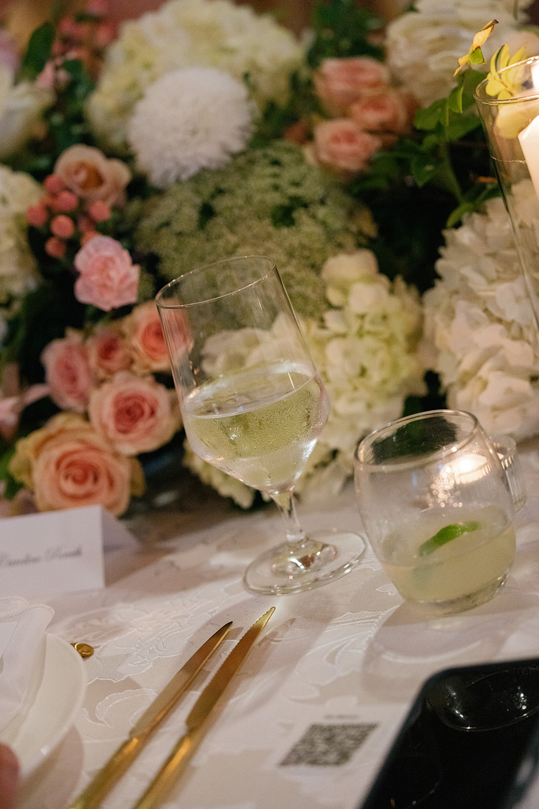 Elegant floral centerpiece of roses, hydrangeas, and greenery on a candlelit reception table with drink glasses at Huguenot Loft.