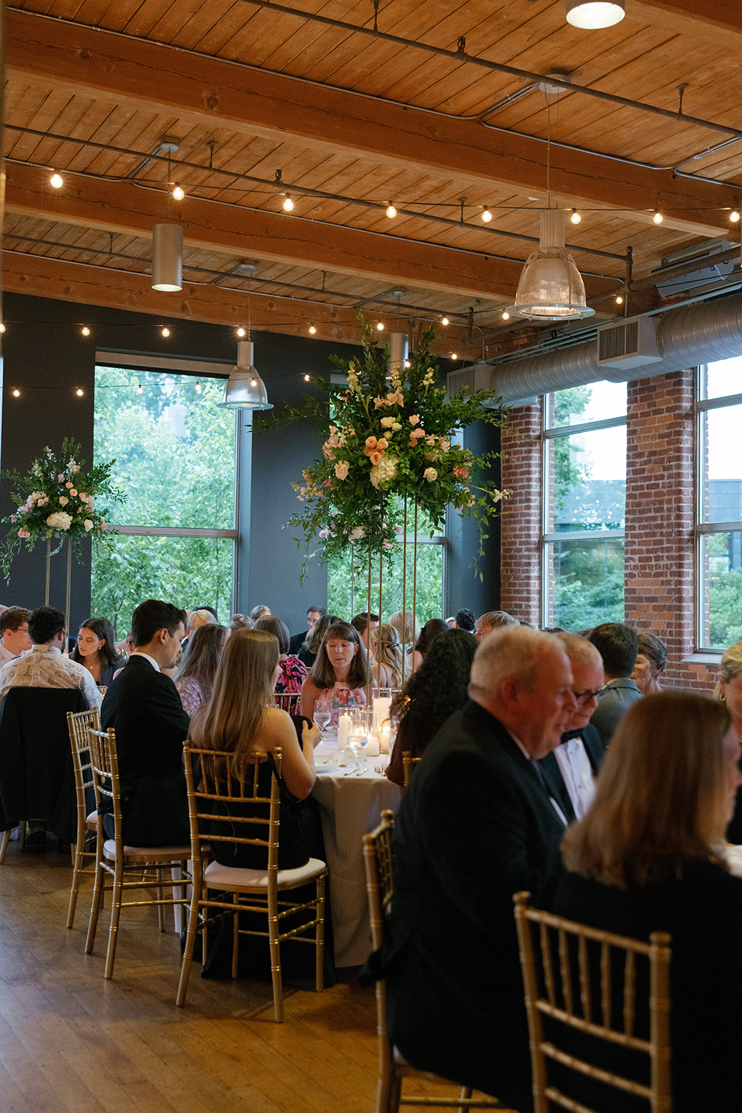 Guests seated at round tables with lush floral arrangements and golden chiavari chairs during a Greenville SC wedding reception.