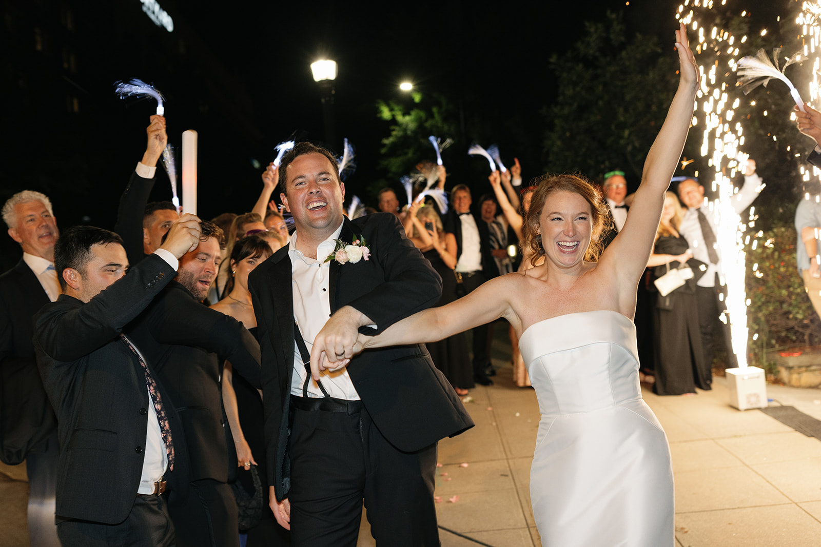 Wedding guests cheer with light-up wands as the bride and groom make their grand exit, surrounded by excitement and sparkler fountains.