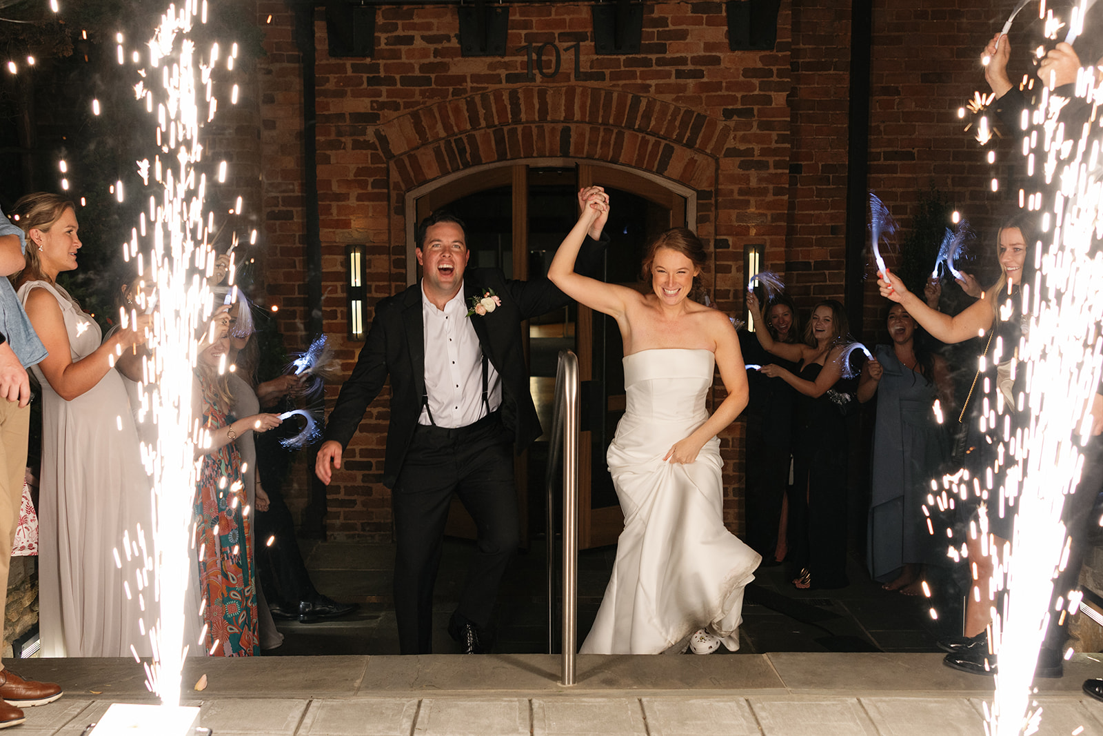Bride and groom holding hands and running through cold spark fountains outside Huguenot Loft for their wedding grand exit.