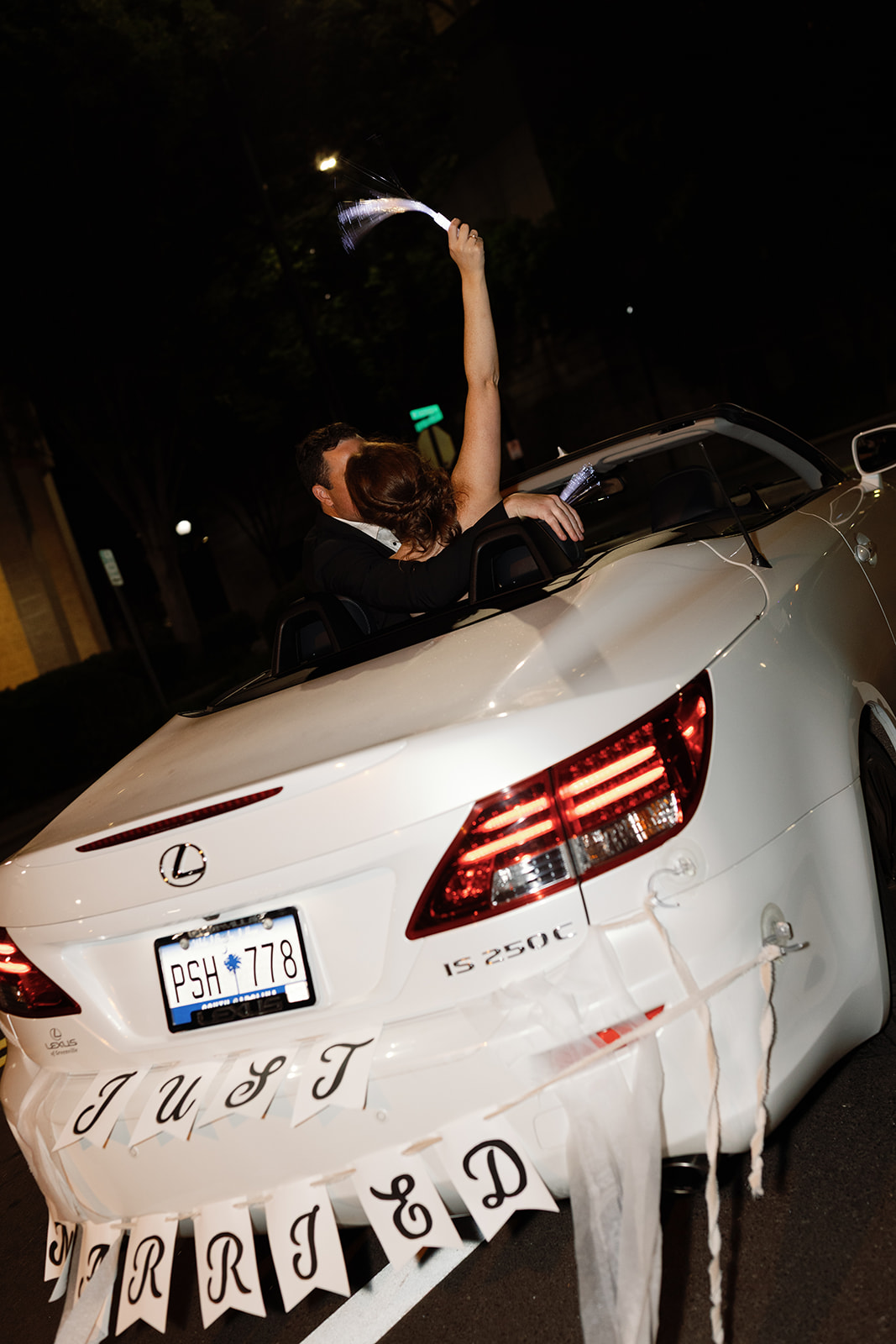 Bride and groom share a kiss in a white convertible with “Just Married” sign as they drive away from their Greenville SC wedding.