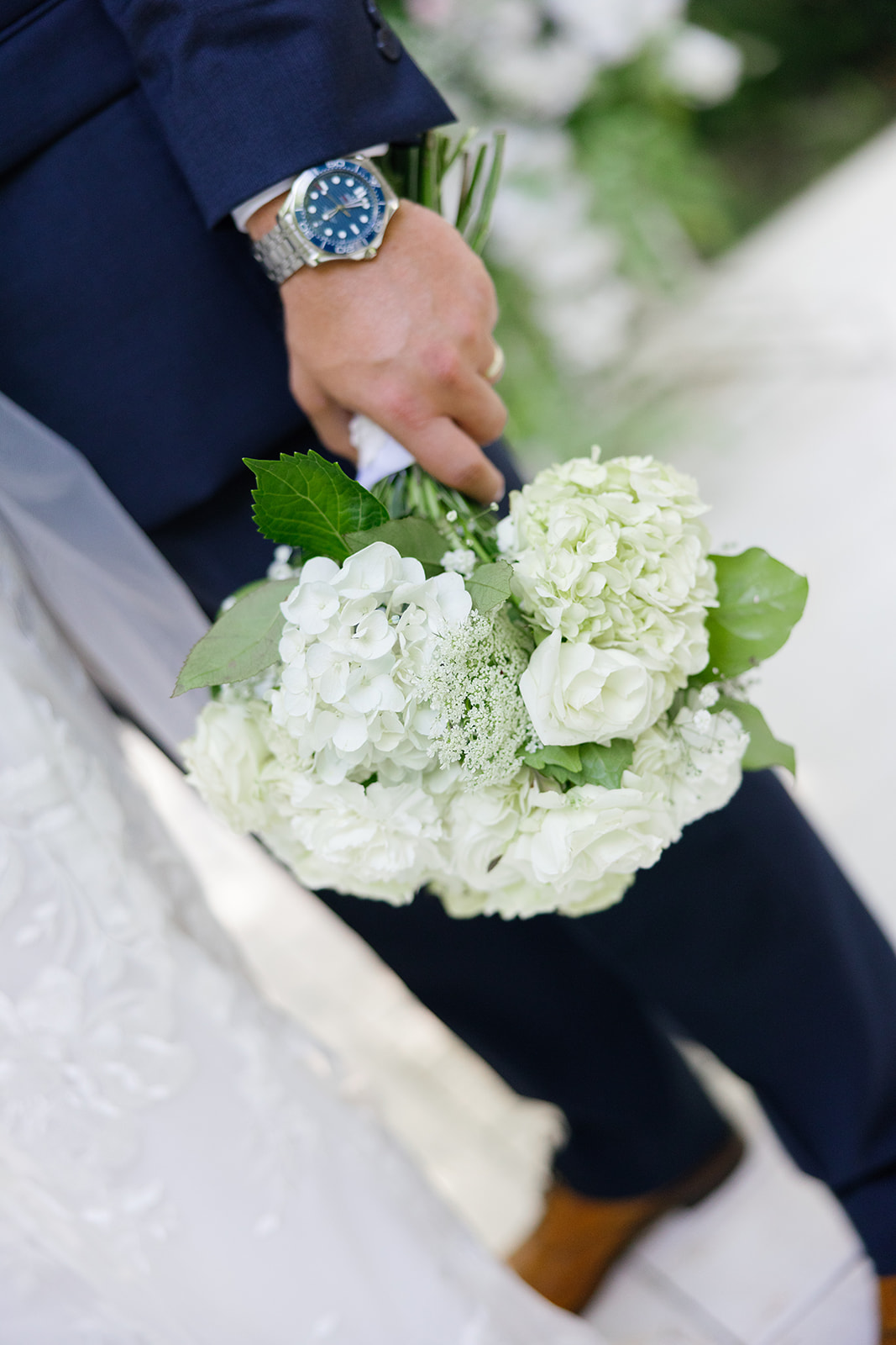 Close-up of groom holding the bride’s bouquet of white flowers.