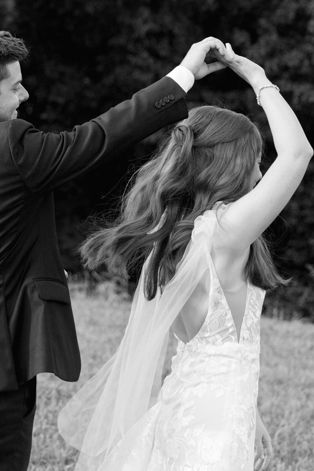 Black and white photo of the groom twirling the bride as her veil flows behind her.