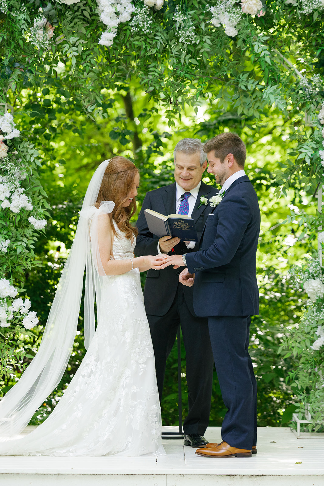 Bride smiling while placing the wedding ring on the groom’s finger during the ceremony.